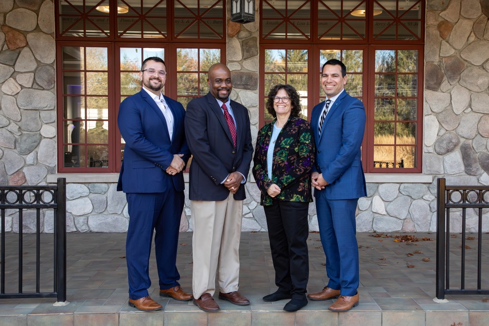 Four award recipients pose and rotate together outside of Alumni House